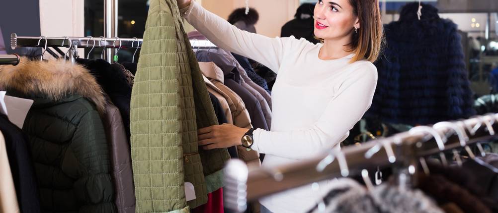 Steppjacke für Damen im Test: Frau in weißem Oberteil hält eine grüne Steppjacke hoch und betrachtet diese.