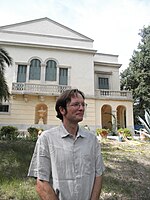 Le chercheur est photographié en contre plongée avec dans le fond le Plantier. Chemise blanche lunettes.