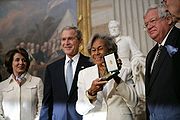 Rachel Robinson accepting the Congressional Gold Medal for her husband, deceased baseball star Jackie Robinson. From left to right: Congresswoman Nancy Pelosi, former President George W. Bush, Rachel Robinson, Congressman Dennis Hastert (2 March 2005)