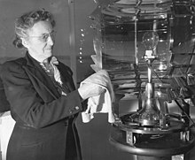 An older woman polishes the mirror, known as a Fresnel lens, behind a light bulb