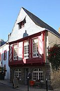 Vue d’une maison en granit, pans de bois rouges en façade, toit en ardoises.