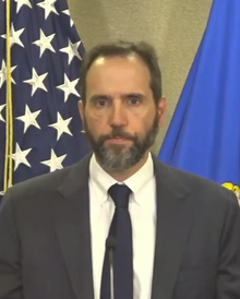 Smith standing in front of flags, wearing a suit