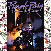 Prince on a purple motorcycle with Apollonia standing in front of a building behind him with the door open. Various flowers appear in the sides with a white background.