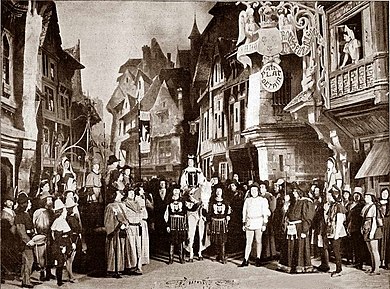 photograph of stage, large cast in 16th century costumes, open-air scene outside an inn, man on horse at centre