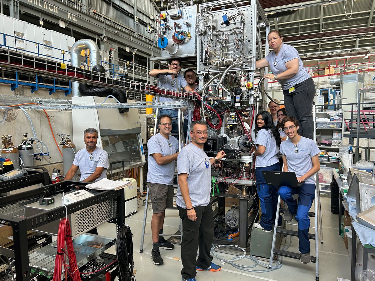 A group of lab workers in matching tee shirts posing together around a fusion machine. 