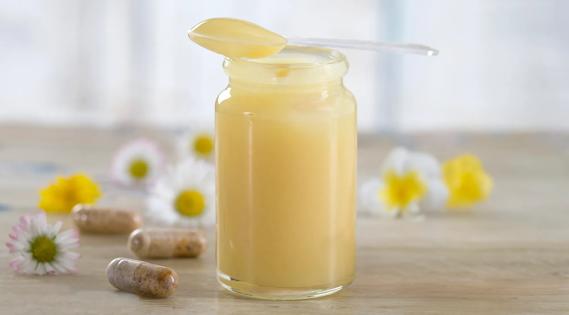 Jar of royal jelly with spoon on top, with capsules and flowers on table