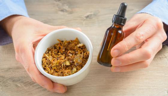 Hands holding small bowl of propolis and dropper bottle of liquid propolis