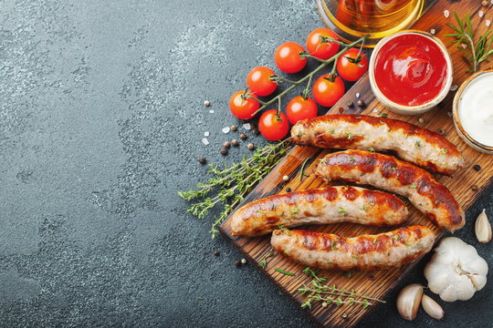 Fried sausages with sauces and herbs on a wooden serving Board. Great beer snack on a dark background. Top view with copy space