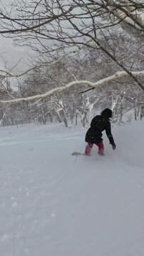 VERTICAL: Snowboard rider sprays through deep powder snow among snowy trees in a tranquil winter forest. Exciting experience and pleasure of backcountry snowboarding in Japanese winter fairy tale.