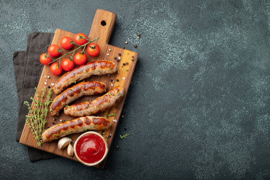 Fried sausages with sauces and herbs on a wooden serving Board. Great beer snack on a dark background. Top view with copy space