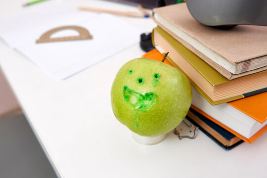 Green apple with face holes near school books on a table