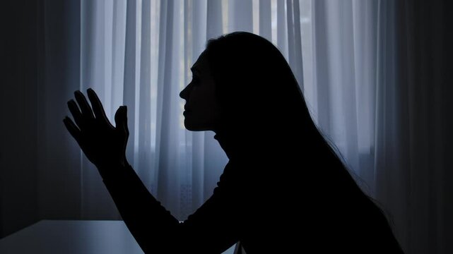 Silhouette of woman sitting at table in front of window, disappointed depressed expression, mental crisis, exhausted frustrated mood. Human emotions and mental health.