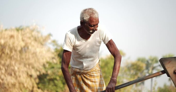 View of an old Indian man using handpump at rural countryside.