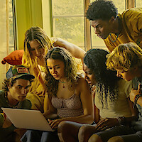 The cast of Outer Banks gathered around a laptop