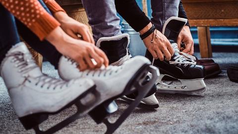 Beine mit Schlittschuhen bekleidet, die gerade von Händen geschnürt werden.