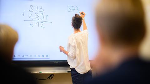 Lehrerin an digitalem Whiteboard macht Matheaufgaben vor Kindern, die sich melden