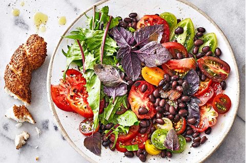 Tomaten-Bohnensalat auf weißem Teller mit Feta und angebrochenem Simit