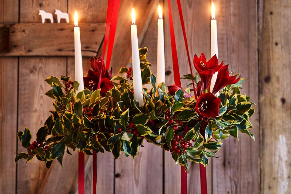 Hängender Adventskranz mit roten Schleifen und Ilex vor Holzwand