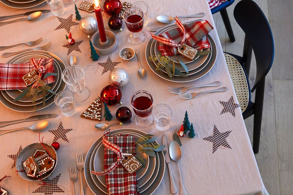 Ein festlich gedeckter Tisch, dekoriert mit Kugeln, Lebkuchen, Kerzen und karierten Papiersternen