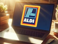 Laptop steht mit Aldi-Logo auf dem Display auf einem Schreibtisch im Sonnenlicht.