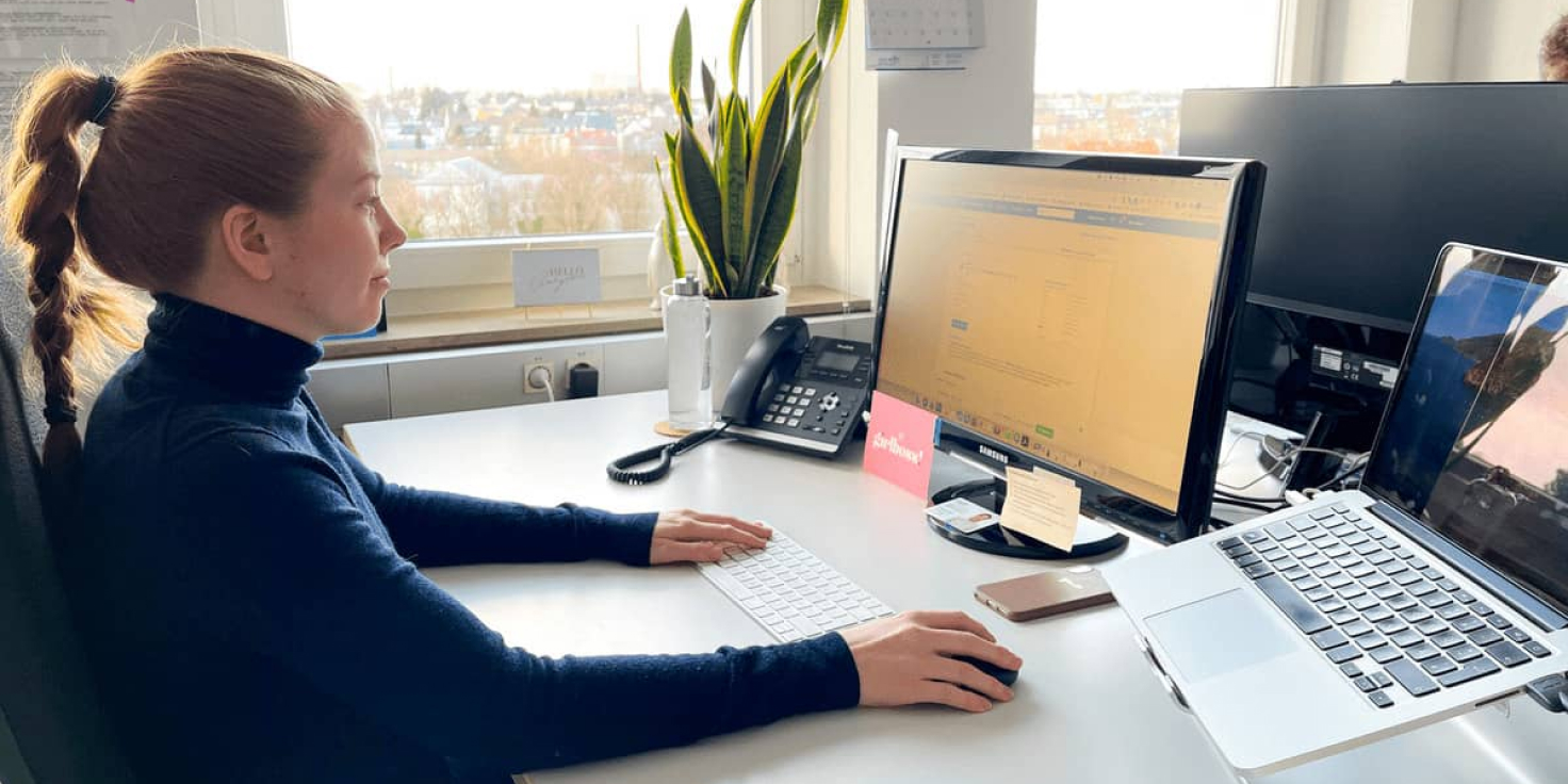 aweos Frau arbeitet an einem Schreibtisch mit zwei Monitoren und einem Laptop