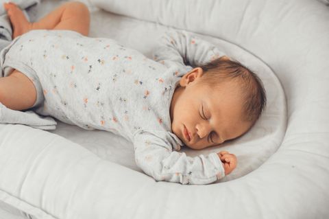 Babynest: Baby im grauen Body macht ein Nickerchen im Kuschelnest.