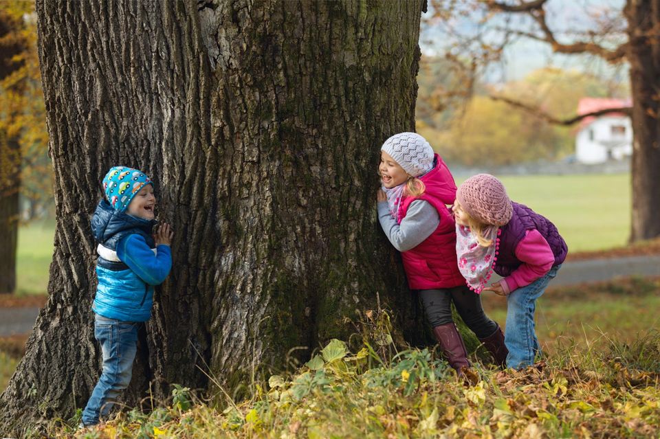 Alte Kinderspiele: Drei Kinder spielen um einen alten Baum herum