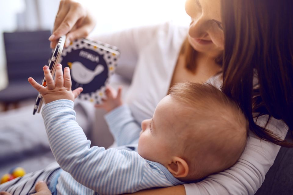 Babybücher: Baby liegt auf Arm der Mutter und greift nach Buch