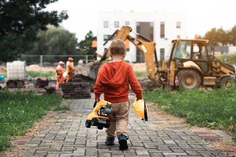 Ein kleiner Junge mit Spielzeug-Bagger und Helm in der Hand