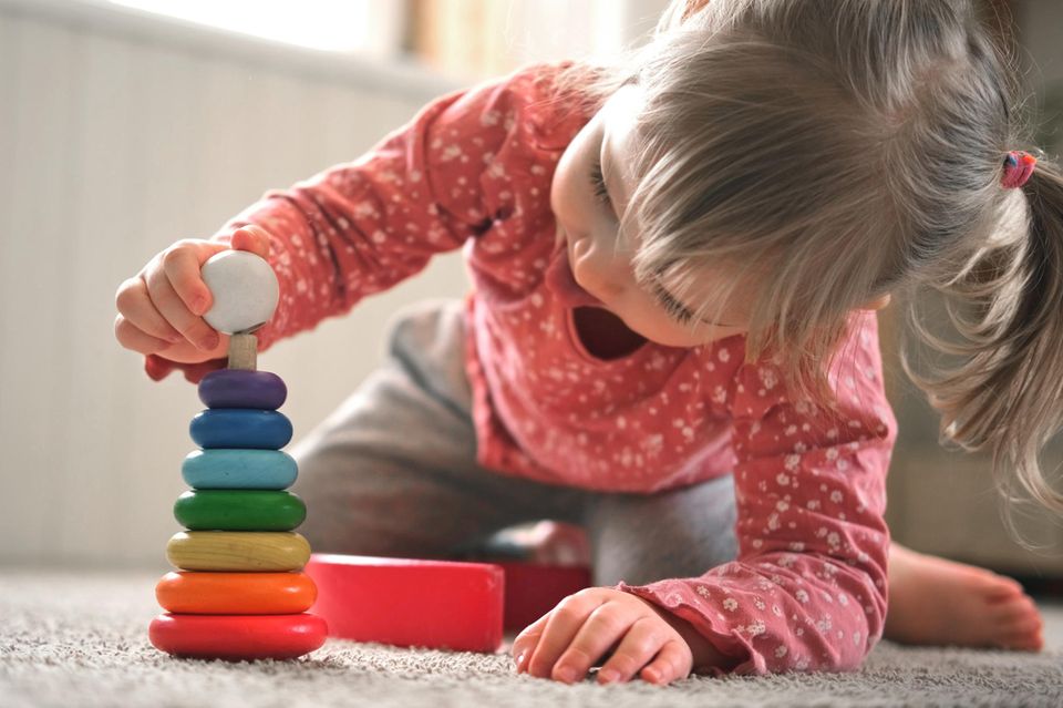 Spielzeug für 3-Jährige: Mädchen spielt konzentriert mit Stapelturm.