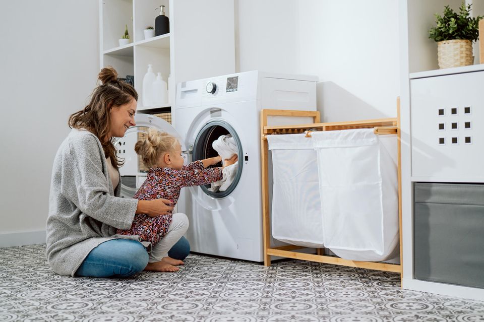 Waschmaschinen im Test: Eine Mutter sitzt mit ihrer Tochter vor einer Waschmaschine.