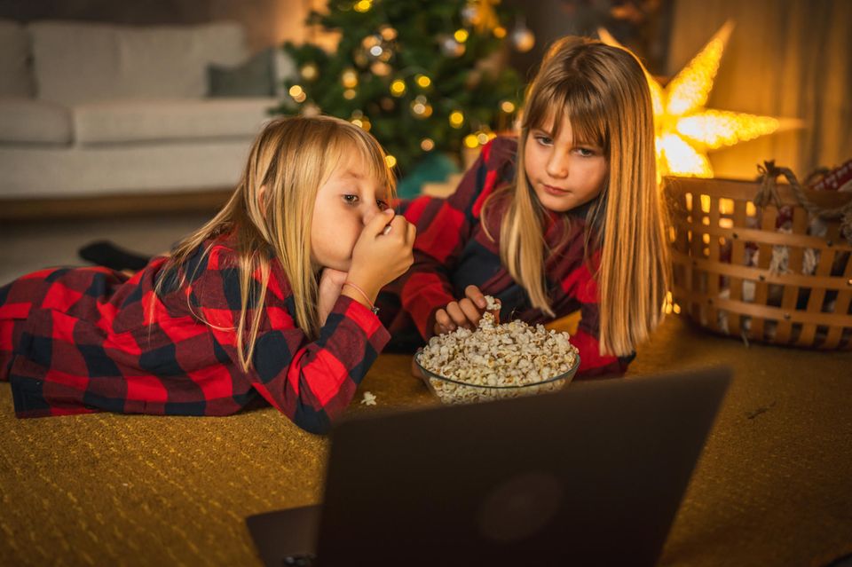 Zwei Kinder liegen auf dem Boden vor einem Laptop und essen Popcorn