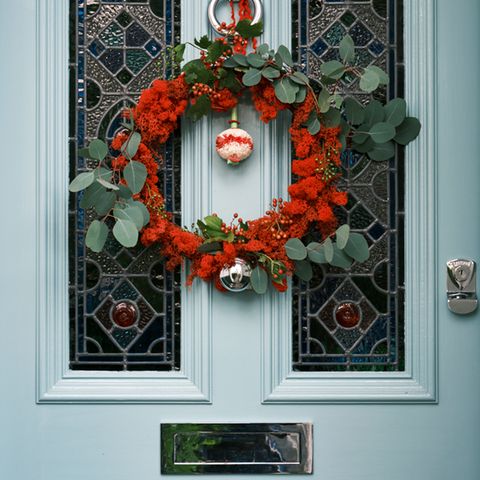 Weihnachtskranz in Rot mit Eukalyptuszweigen, Silberkugel und Beeren an einer hellblauen Tür mit Buntglas