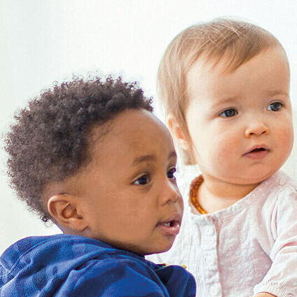 Das Bild zeigt zwei Kleinkinder, ein Mädchen und ein Junge, die Ihren Blick zum rechten Bildrand richten.