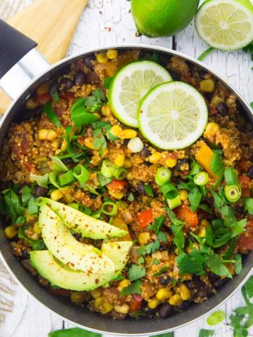 One Pan Mexican Quinoa in a black pot on a white wooden countertop with limes and parsley on the side