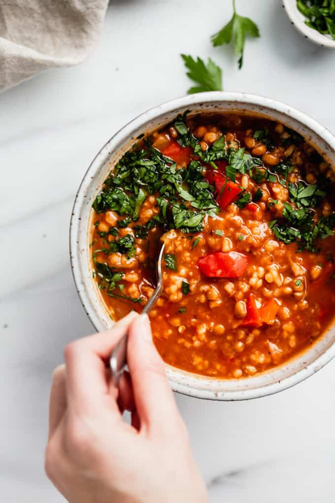 a bowl with vegan stuffed pepper soup on a marble counter top with a hand holding a spoon 