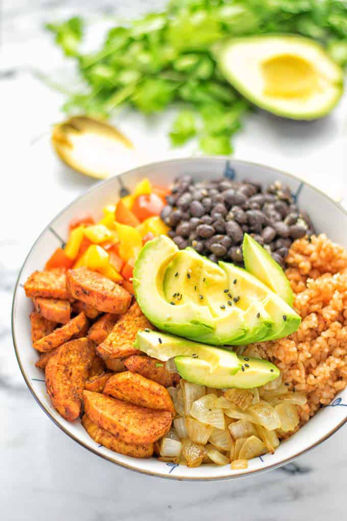 a Cajun sweet potato rice bowl on a marble counter top with fresh cilantro and an avocado half in the background 