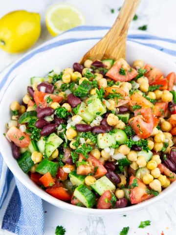 Chickpea Salad in a white bowl with a wooden spoon and two lemons in the background