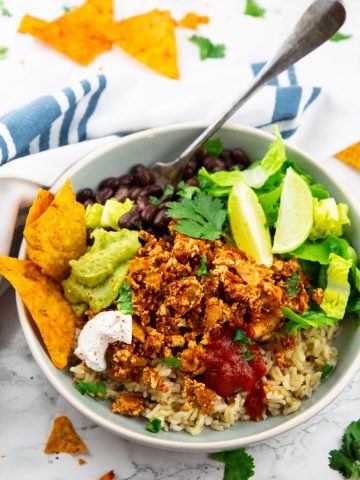 a grey bowl with brown rice, lettuce, guacamole, and sofritas with a fork