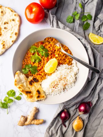 vegan dal with rice in a white bowl with a spoon on a marble countertop