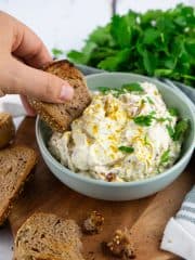 a hand dipping a piece of bread into a bowl of vegan dip