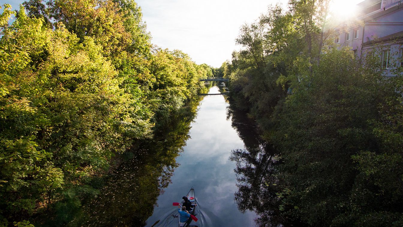 Das Bild zeigt ein Kanu auf dem Karl-Heine Kanal, der links und rechts von grünen Bäumen und Sträuchern umgeben ist.