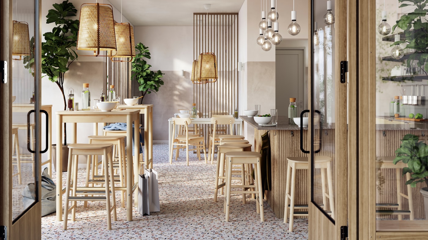 A light, airy restaurant with tidily arranged RÖNNINGE birch bar tables and bar stools under KNIXHULT bamboo pendant lamps.