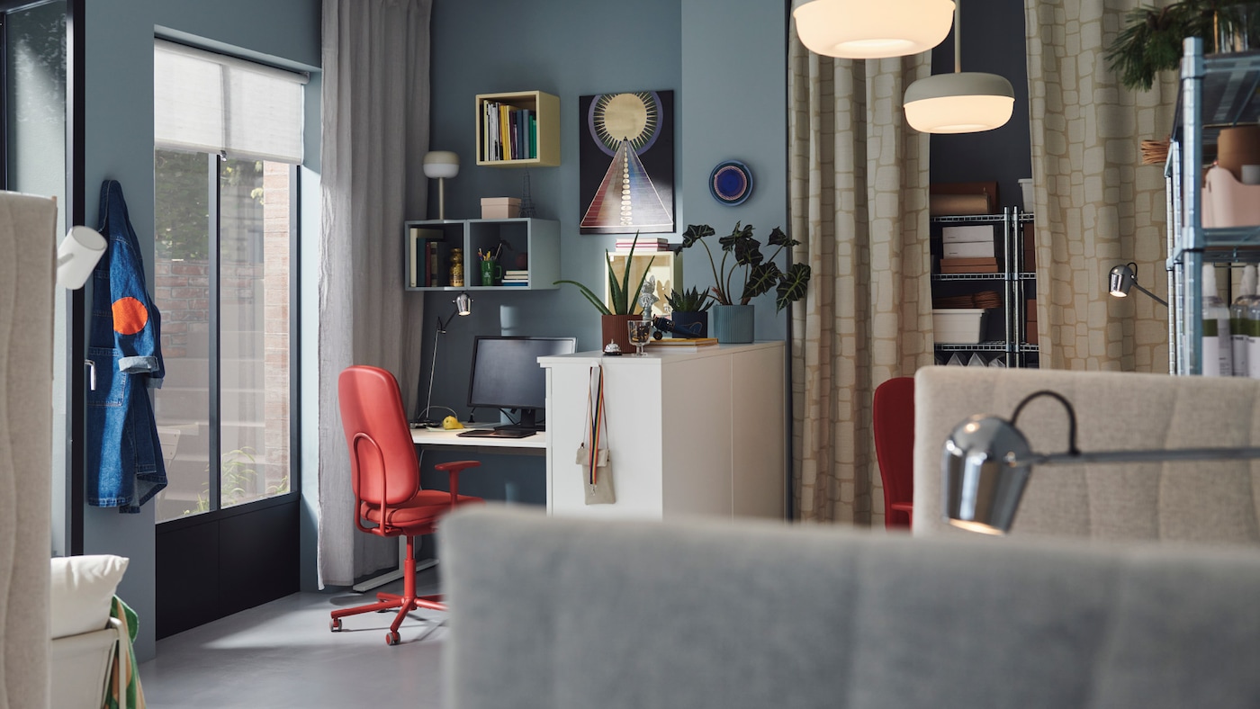 A vibrant office space with blue walls, wall-mounted cabinets in various colours, and SMÖRKULL office chairs in Gräsnäs red.