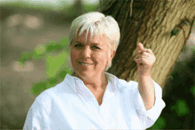 a woman in a white shirt is smiling and pointing at the camera