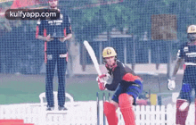 a group of cricket players are playing a game of cricket on a field with a net in the background .