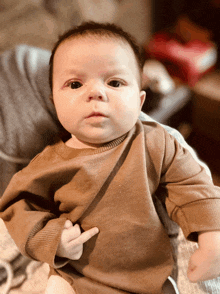 a baby in a brown shirt is making a middle finger gesture