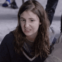 a girl with long hair is wearing a blue sweater and making a funny face