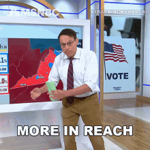 a man in a white shirt and tie holds a piece of paper in front of a sign that says vote