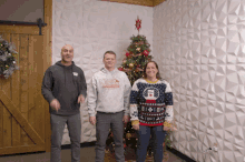 three people standing in front of a christmas tree one of whom is wearing a sweater that says " ugly christmas sweater "